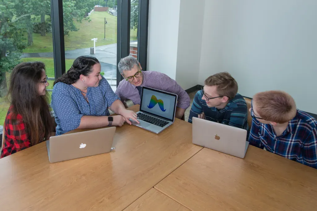 A professor reviews a student's graph in a classroom with three other students